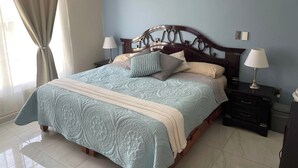 A bedroom with a bed, two bedside tables, a nightstand, a lamp, a curtain, and a wall switch. - Beautiful, modern 2-bedroom home located on a private street. (Teoloyucan)