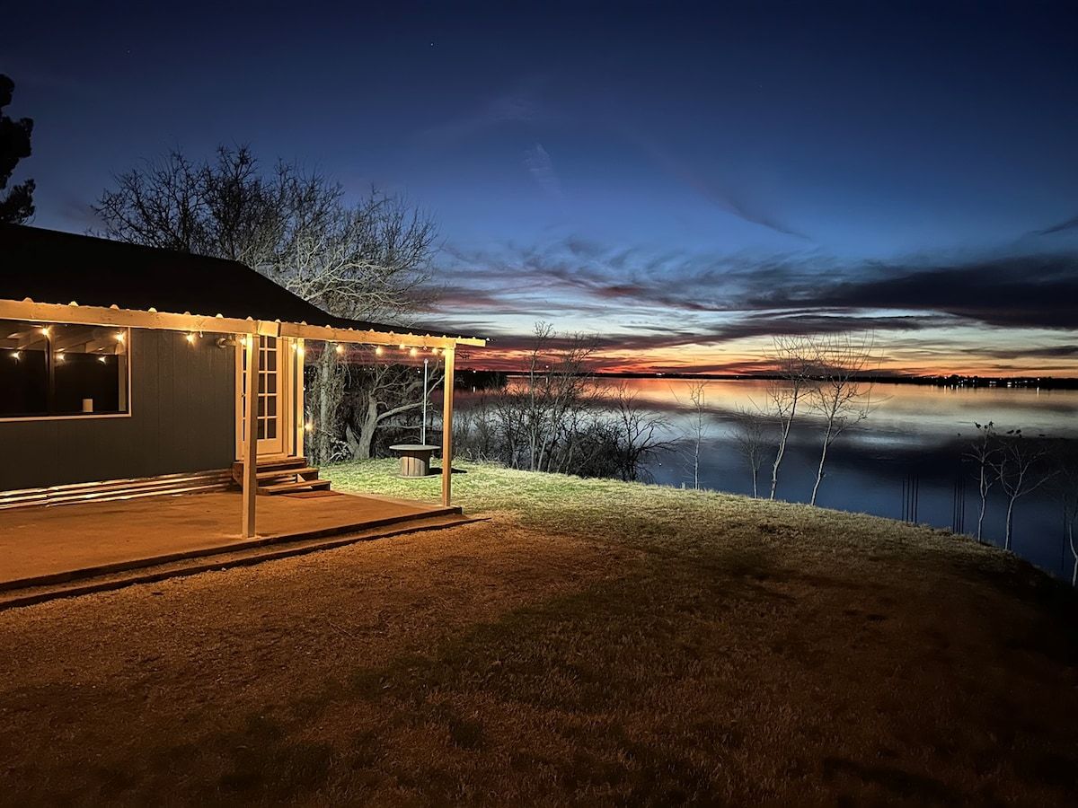 A house with a covered porch, a lawn, and a body of water in the background.