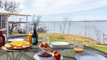 Un petit-déjeuner composé de gaufres, d’œufs, de fruits rouges et de jus, servi sur une table près d’un lac.