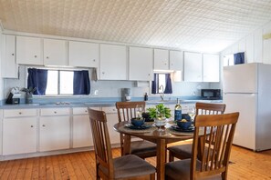 A compact kitchen with white cabinets, a dining table with chairs, and a refrigerator. - Best Sunsets on the Lake! 2-Bed 1-Bath | Gameroom! (Abilene)