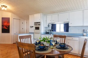A dining area with a wooden table set for four, surrounded by white cabinets and a kitchen area with a stove and oven.
