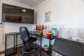 A room with a flat-screen TV mounted on the wall, a black office chair, a popcorn bucket, a bottle of soda, and a glass jar on a table.