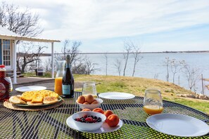 Un petit-déjeuner composé de gaufres, d’œufs, de fruits rouges et de jus, servi sur une table offrant une vue sur un lac.