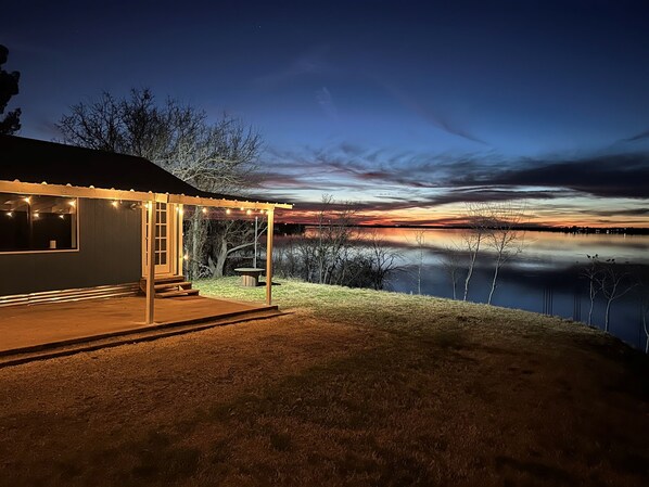 Une maison dotée d’un porche abrité, d’une petite terrasse et offrant une vue sur un lac au crépuscule.
