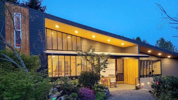 Une maison moderne dotée de grandes fenêtres, d’un revêtement extérieur en bois et d’une allée gravillonnée.