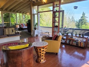 A spacious living area with a wooden floor, a yellow armchair, a round wooden table, and a bookshelf filled with books. - Mountain View Hideaway (Seattle)