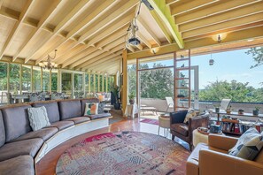 A spacious living area with a curved sofa, a round rug, and a view of the outdoors through large windows. - Mountain View Hideaway (Seattle)