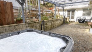A hot tub in a backyard with a pergola, a wooden fence, and a house in the background. - Near Bass Lake | Harley`s Hideaway Suite | Hot Tub (Oakhurst)