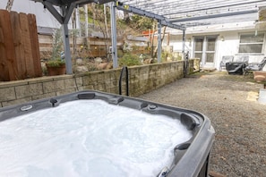 Un jacuzzi en un patio trasero con una pérgola, una valla de madera y una casa al fondo.