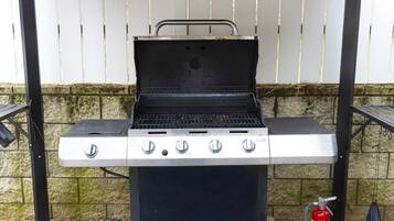 A barbecue grill with four burners, a side shelf, and a fire extinguisher nearby.