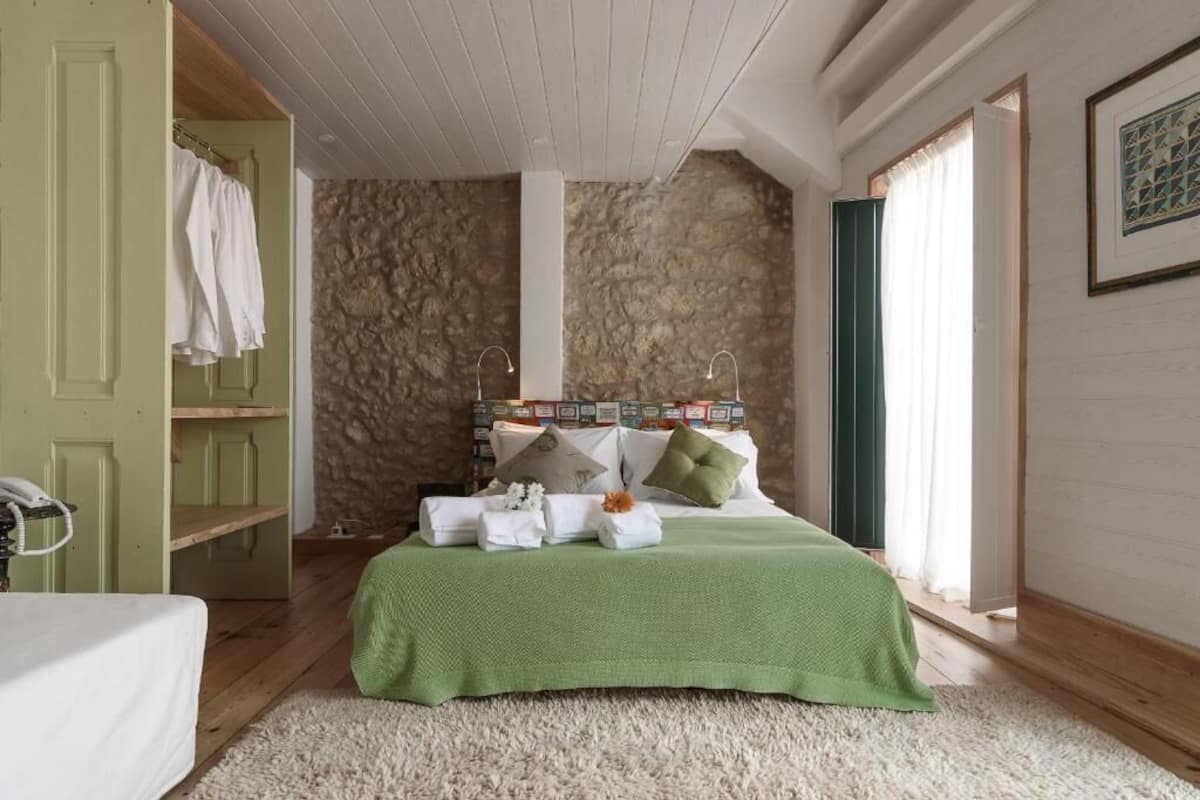 A bedroom with a stone wall, a green bedspread, and a white rug.