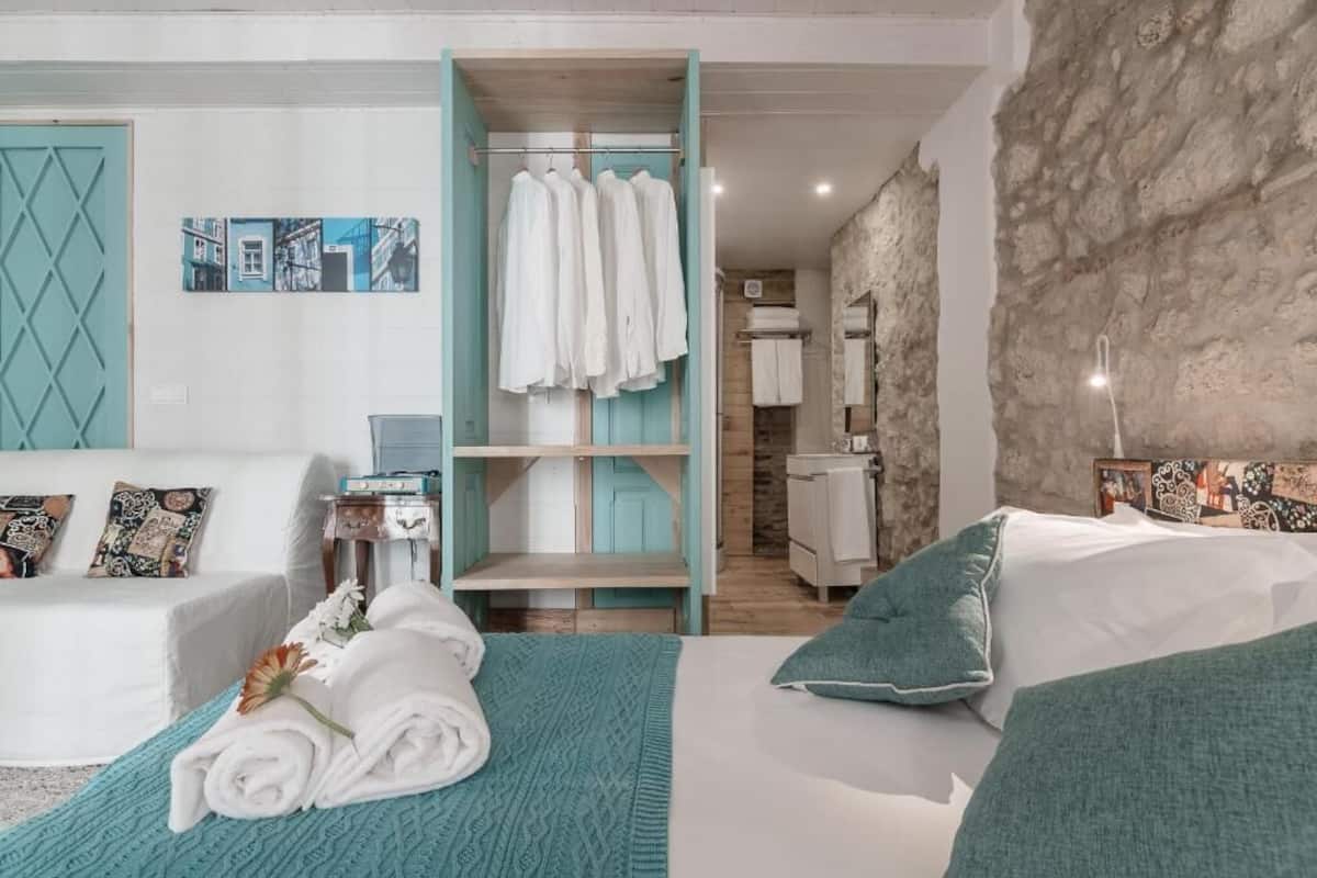 A hotel room with a bed, a seating area with a sofa, a wardrobe, and a bathroom visible through an open door.