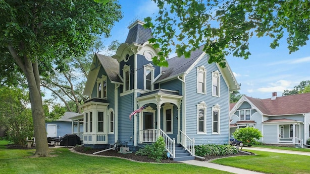 A two-story house with a porch, a chimney, and a flag. - The Ainsworth House - Historic Victorian 3BR Gem (Stoughton)
