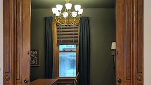 A room with a wooden door frame, a chandelier, a dining table with chairs, a window with blinds, and a rug. - The Ainsworth House - Historic Victorian 3BR Gem (Stoughton)