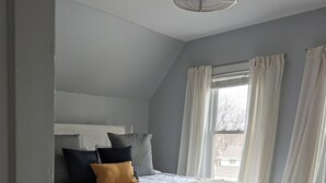 A bedroom with a bed, a window with curtains, a door, and a ceiling light fixture. - The Ainsworth House - Historic Victorian 3BR Gem (Stoughton)