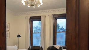 A living room with a sofa, two armchairs, a coffee table, a lamp, and a patterned rug. - The Ainsworth House - Historic Victorian 3BR Gem (Stoughton)