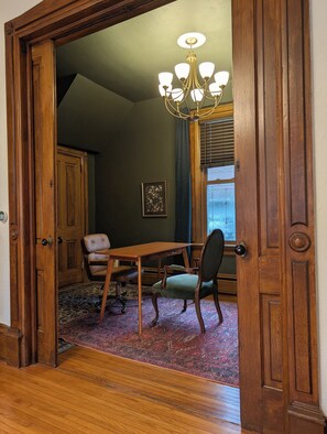 Una habitación con una puerta de madera, una mesa de comedor con sillas, una araña y una ventana con persianas.