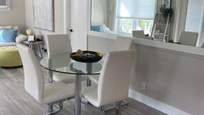 Ein moderner Essbereich mit einem Glastisch und weißen Stühlen, einer Couch mit blauem Kissen und einem großen Spiegel, der den Raum reflektiert.