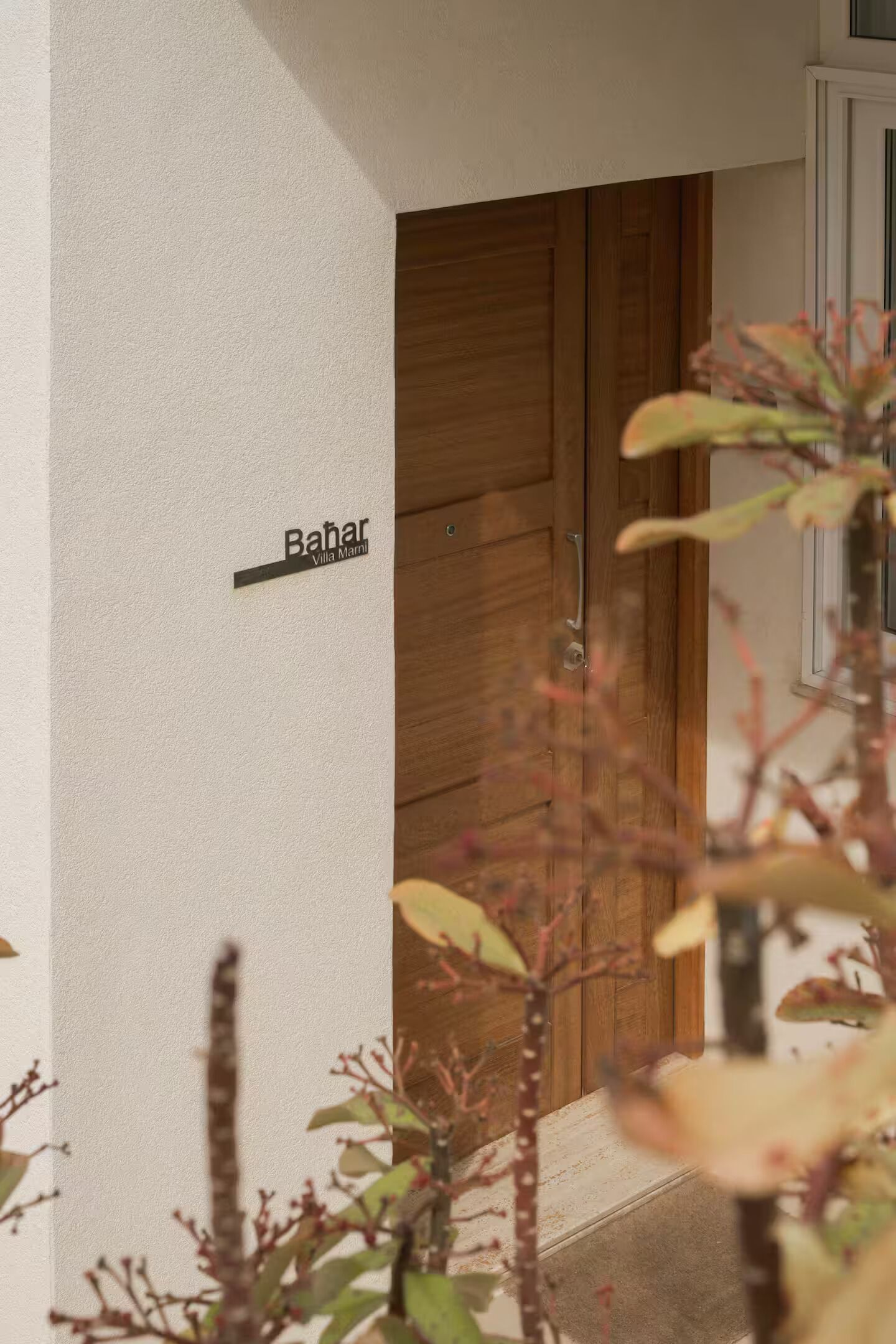A wooden door, a sign reading 'Bahar Villa Marli,' and a plant in the foreground.