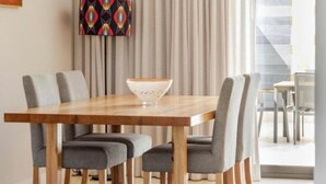 Een eetgedeelte met een houten tafel, vier grijze stoelen, een decoratieve schaal, een kleurrijk abstract schilderij en uitzicht op een trap.