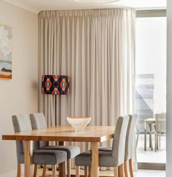 A dining area with a wooden table, four grey chairs, a decorative bowl, a colorful abstract painting, and a view of a staircase.
