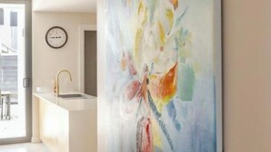 Een moderne keuken met een groot abstract schilderij aan de muur, een inbouwspoelbak en een klok.