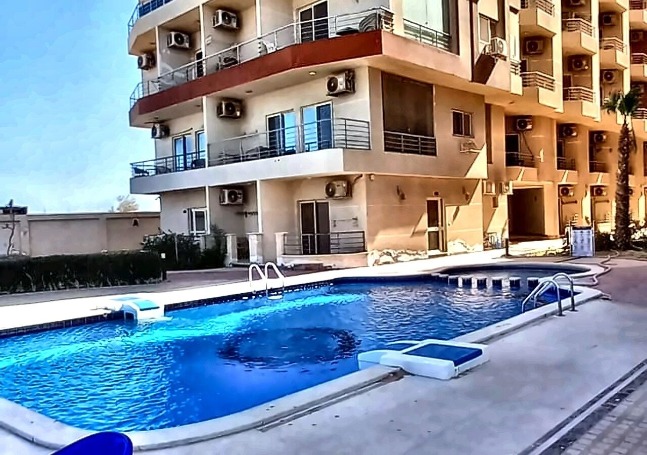 A swimming pool adjacent to a multi-story building with balconies and air conditioning units.