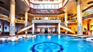 A large indoor swimming pool with a central circular design, surrounded by columns with intricate patterns, and a grand staircase leading to an upper level. - Your perfect Red Sea getaway at Hurghada. (Hurghada)