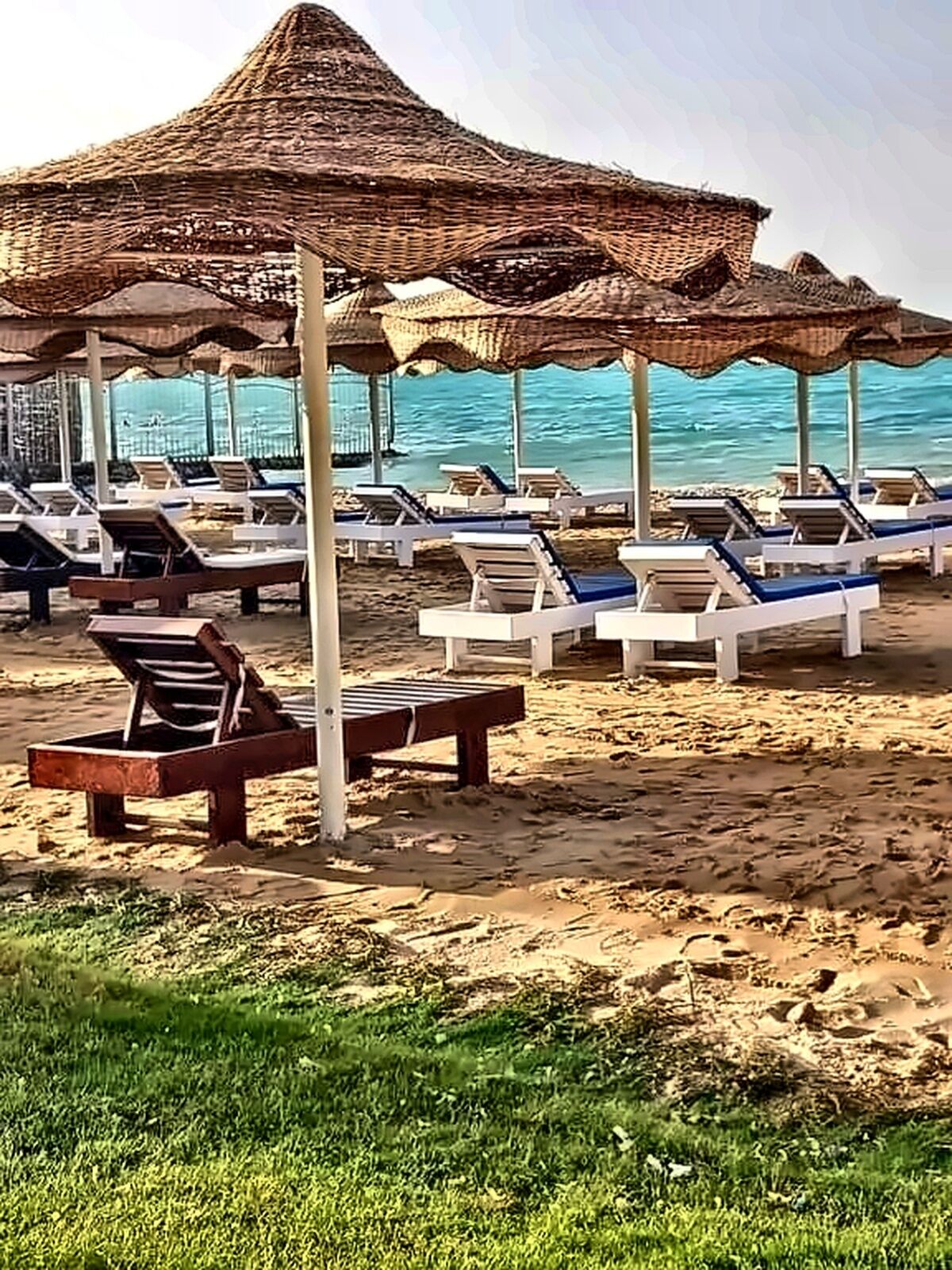 A beach with sun loungers and thatched umbrellas.