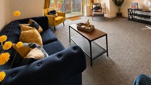 En stue med sofa, sofabord og lænestol. Der er en balkon med udsigt til bygninger.