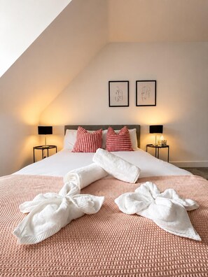 A neatly made bed with a checkered pillow, two bedside lamps, and a framed artwork on the wall.