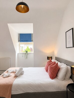 A bedroom with a bed, pillows, a bedside table, a lamp, a window with a view, and a hanging plant. - Garden Relaxation, Easy City Centre Access, Secure Parking, Groups & Families (Nottingham)