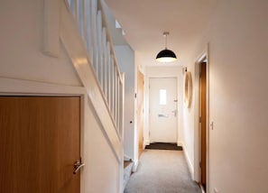 A narrow hallway with a wooden door on the left, a white wall, and a staircase with white railings.