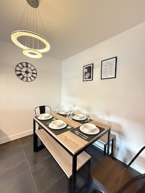 A dining area with a wooden table, black chairs, and a modern light fixture. - Garden Relaxation, Easy City Centre Access, Secure Parking, Groups & Families (Nottingham)