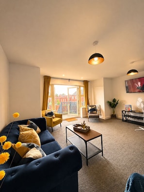 A living room with a sofa, armchairs, a coffee table, and a TV on the wall. - Garden Relaxation, Easy City Centre Access, Secure Parking, Groups & Families (Nottingham)