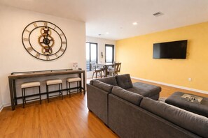 A modern living room with a sectional sofa, a dining area with a table and chairs, and a wall-mounted TV.