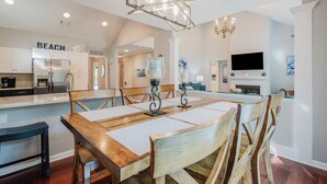 A modern kitchen with a central island, wooden chairs, a chandelier, and a TV mounted on the wall. - Sea Pines Serenity w/pool access & beach shuttle (Hilton Head Island)