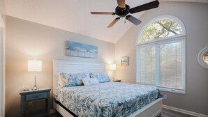 A bedroom with a bed, two bedside lamps, a ceiling fan, a window with blinds, and a painting on the wall. - Sea Pines Serenity w/pool access & beach shuttle (Hilton Head Island)