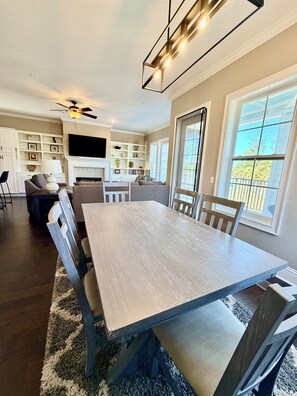 A dining area with a large table, chairs, a ceiling fan, and a TV in the background. - Marvelous 3-bedroom townhome with Pool, Boat Ramp and River Views (St. Marys)