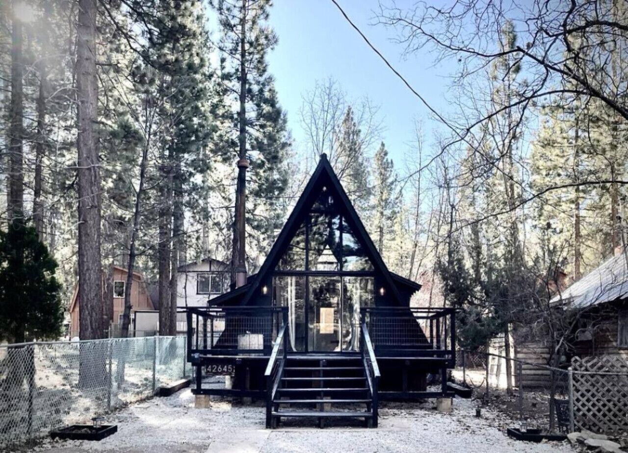 Une cabane avec un toit triangulaire, un escalier menant à l’entrée et une zone délimitée par une clôture.