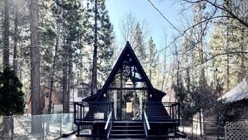 Une cabane avec un toit triangulaire, un escalier menant à l’entrée et une zone délimitée par une clôture.
