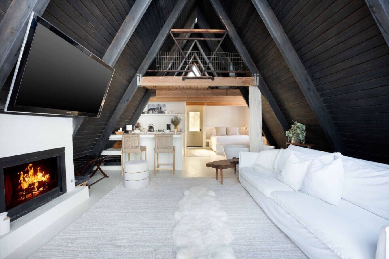 Une pièce de style loft avec une cheminée, un canapé blanc et un coin cuisine à l’arrière-plan.