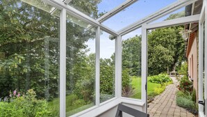 A conservatory with a view of a garden, a bench, and a pathway leading outside. - Charming Riverside Cottage in the Heart of Pembrokeshire (Cosheston)