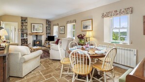 A cozy living room with a fireplace, a dining area with wooden chairs, a sofa, and a bookshelf. - Charming Riverside Cottage in the Heart of Pembrokeshire (Cosheston)
