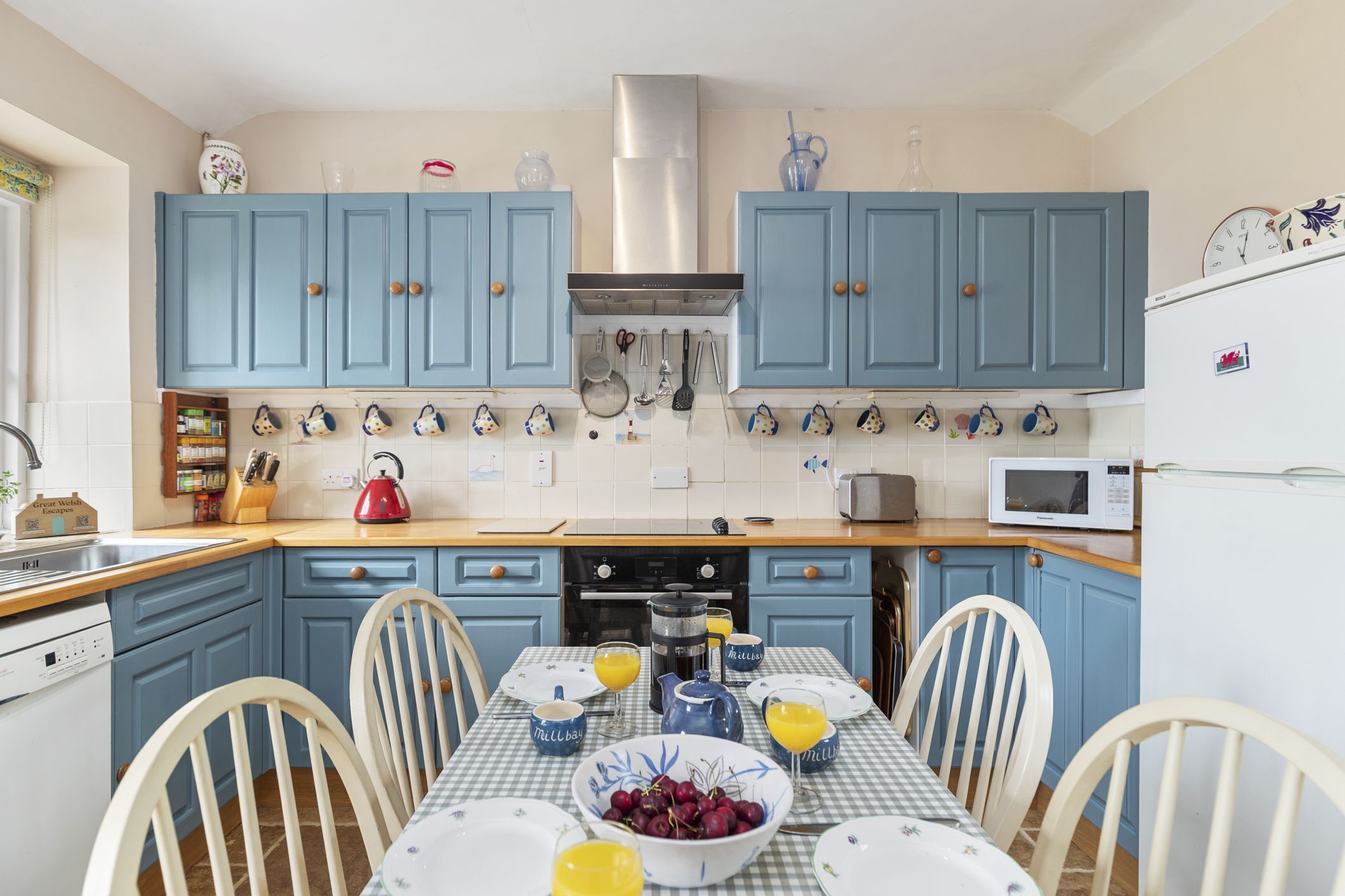 A kitchen with blue cabinets, a microwave, a kettle, and a table set for breakfast.