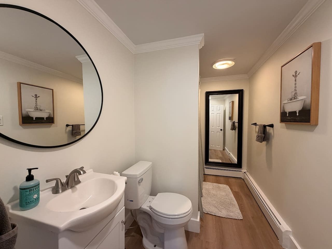 Een badkamer met een witte wastafel, toilet en spiegel. Er is een handdoekhouder aan de muur en een vloerkleed op de grond.