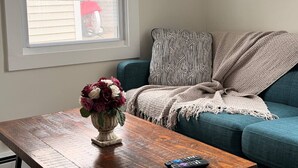 A living room with a wooden coffee table, a blue sofa, a patterned throw blanket, and a vase with flowers. - Tiny, Budget Friendly 1 Bedroom Central CT (Southington)