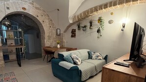 Een woonkamer met een blauwgroene bank, een houten bureau en een stenen boog.