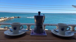 Een tafel met twee koffiekopjes en een koffiepot op een houten terras met uitzicht op de zee.