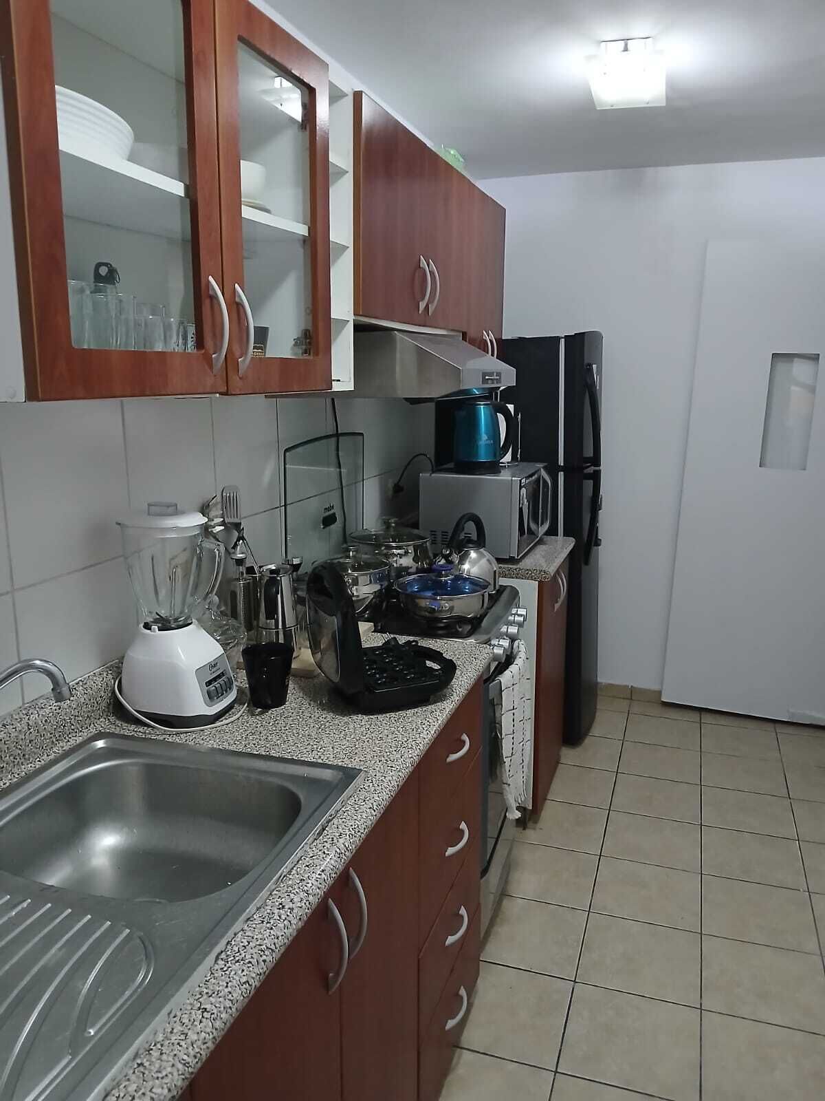 Een keuken met een spoelbak, een blender, een koffiezetapparaat, een magnetron en een koelkast.